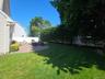 Expansive green lawn, paver patio, established privacy hedging, mature trees, and a white privacy fence
