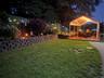 Lawn area with a block retaining wall, landscaped garden beds, and an illuminated covered deck