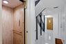 Wood-finish interior elevator with control panel and handrail, alongside a hallway featuring high-gloss flooring, a dark-stained staircase, and a pane