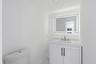 White vanity with textured cabinet doors and dark hardware, integrated rectangular sink, wall-mounted faucet, and illuminated mirror