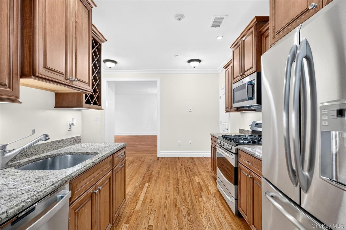 Kitchen featuring wood-finish flooring, granite countertops, stainless steel appliances, and wood cabinetry with a built-in wine rack