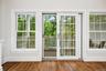 Rich wood-finish flooring, white trim, and multiple windows with muntin bars
