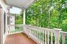 Outdoor balcony with wood-finish decking, white baluster railing, and a columned support