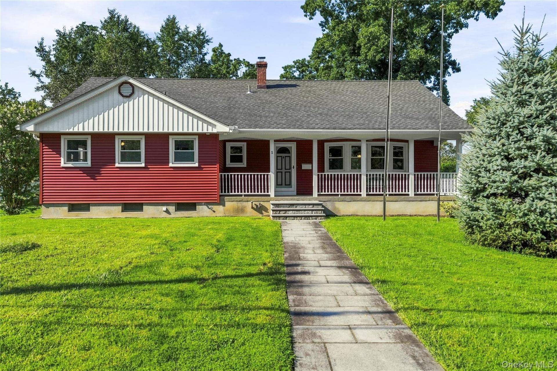 Red-sided residence featuring a covered front porch with white railings, a front-facing gable with vertical siding, and a stone-paved walkway