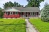 Red-sided residence featuring a covered front porch with white railings, a front-facing gable with vertical siding, and a stone-paved walkway