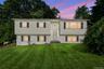Raised ranch residence featuring a light-toned exterior, multiple windows with dark shutters, and a prominent front entrance with a storm door