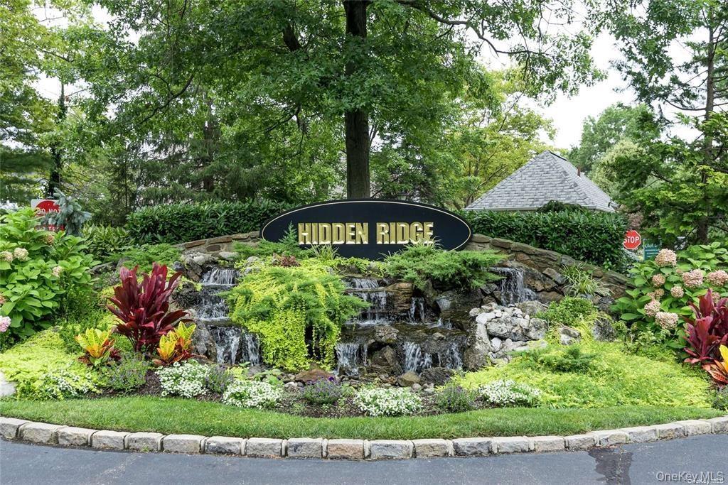 Decorative community entry sign with a cascading water feature, stone surround, and diverse planted foliage