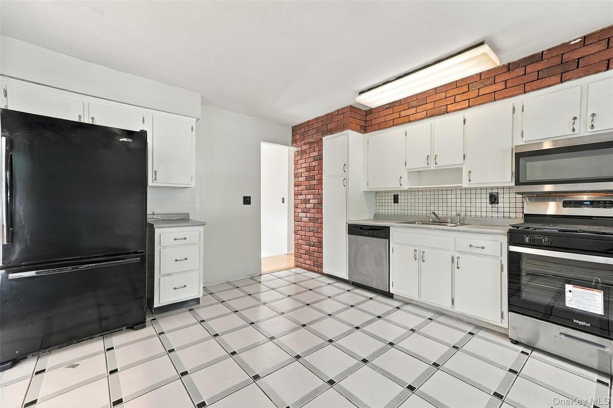 Kitchen featuring white cabinetry, a tile backsplash, stainless steel appliances, and a brick accent wall
