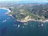 Aerial perspective of coastal landscape featuring rugged cliffs, expansive ocean frontage, sandy shorelines, and dense native vegetation