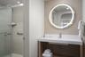 Modern vanity with a seamless integrated sink, wall-mounted circular LED mirror, glass-enclosed shower, and neutral patterned wall tile