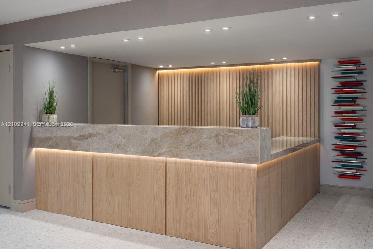 Reception desk featuring wood-paneled cabinetry, a stone-surfaced countertop, integrated under-counter lighting, and a vertical wood slat accent wall 