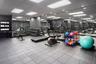 Fitness area featuring wall-to-wall mirrors, industrial-style tile flooring, recessed panel lighting, and built-in storage shelving