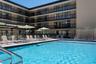Swimming pool with integrated stainless steel ladder, expansive concrete deck, metal perimeter fencing, and multi-story building facade featuring priv