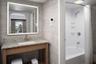 Bathroom featuring a stone-top vanity with an integrated rectangular sink, wall-mounted illuminated mirror, large-format tile wall surfacing, and a sh