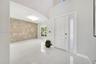 Foyer featuring high ceilings, large-format tile flooring, a prominent textured brick accent wall, and a solid-core entry door with a frosted glass si