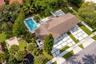 Aerial perspective of a property featuring an in-ground swimming pool, extensive paver hardscaping with geometric inlay, mature landscape, and a fence