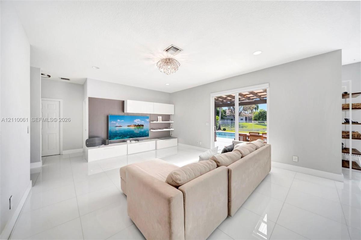 Open-concept living space featuring high-gloss tile flooring, recessed lighting, built-in media cabinetry with floating shelving, and sliding glass do