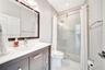 Bathroom featuring a dark-finish vanity with a rectangular sink, quartz countertop, framed wall mirror, and a walk-in shower with sliding glass doors 