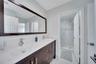 Dual-sink vanity with dark wood-finish cabinetry, solid-surface countertop, full-width mirror, and walk-in glass shower enclosure