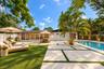 Rear exterior featuring a swimming pool, large-format paver patio with turf inlays, mature palm trees, and full-height glass sliding doors