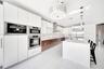 Kitchen featuring two-tone flat-panel cabinetry, a central waterfall-edge island, stainless steel built-in double wall ovens, a coordinating microwave