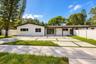 Single-story exterior featuring white stucco siding, a concrete paver driveway with turf accents, a covered porch, and privacy fencing