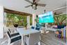 Covered outdoor living area featuring wood-finish tile flooring, ceiling fans with integrated lighting, and white structural columns
