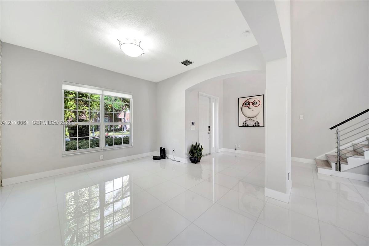 High-gloss tile flooring, arched architectural opening, multi-pane window, and staircase featuring a metal railing system