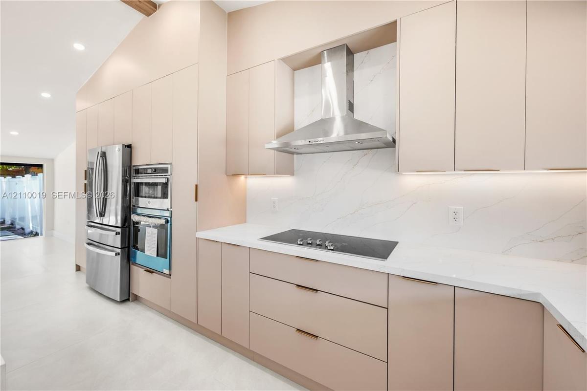 Custom flat-panel cabinetry, stone-surface countertops, full-height stone backsplash, stainless steel built-in double wall ovens, and stainless steel 