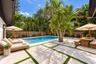 In-ground swimming pool with steps, surrounded by light-toned rectangular stone pavers and synthetic turf inlay, enclosed by a wood-slat perimeter fen