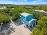 Two-story elevated coastal residence featuring a metal roof, wraparound exterior staircases, covered ground-level parking, gravel driveway, and a priv