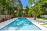 In-ground swimming pool with built-in stairs, bordered by a concrete paver patio with turf inlay, white river rock accents, and mature palm trees