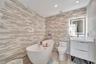 Bathroom featuring floor-to-ceiling multi-tonal linear tile walls, a freestanding soaking tub with handheld sprayer, a vanity with a white countertop 