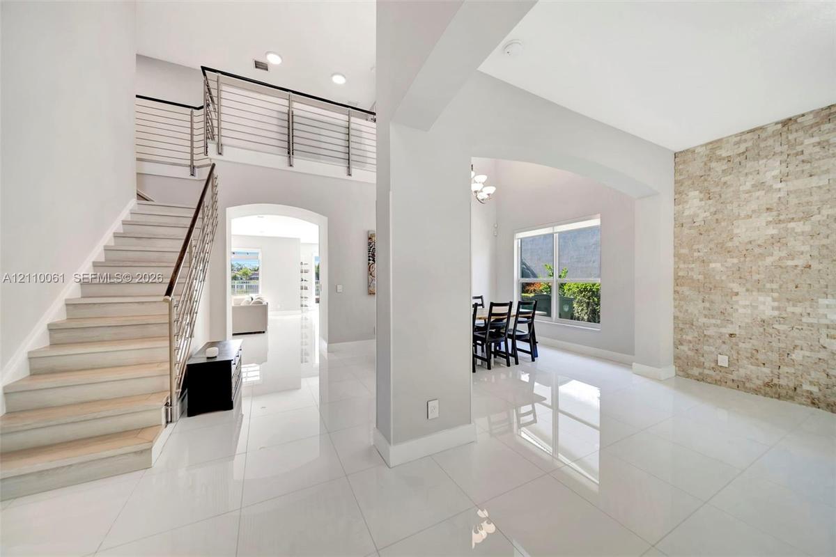 Open-concept interior featuring large-format tile flooring, a floor-to-ceiling textured stone accent wall, a staircase with custom metal railing, and 