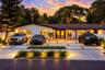 Single-story residence featuring a low-pitched roofline, light-toned exterior finish, segmented concrete driveway with grass inlays, and mature landsc