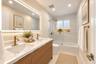Dual-sink vanity with wood-finish cabinetry, quartz countertop, recessed lighting, integrated LED-backlit mirror, and brushed gold-tone fixtures