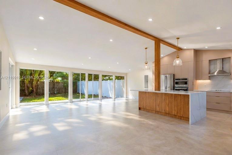 Open-concept space featuring an exposed wood structural beam, floor-to-ceiling sliding glass doors, a large kitchen island with stone-finish waterfall