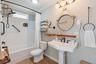 Bathroom featuring white subway tile tub surround, pedestal sink with multi-handle oil-rubbed bronze faucet, round wall-mounted mirror, wood-finish fl