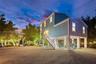 Elevated two-story residence with horizontal siding, gravel ground-level surfacing, metal staircase with railing, and pilings foundation