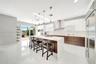Contemporary kitchen featuring an expansive waterfall-edge island, two-tone cabinetry with gloss-finish uppers, stainless steel professional-grade app