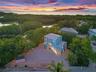 Two-story residence featuring a metal roof, elevated structural foundation, gravel grounds, and perimeter fencing