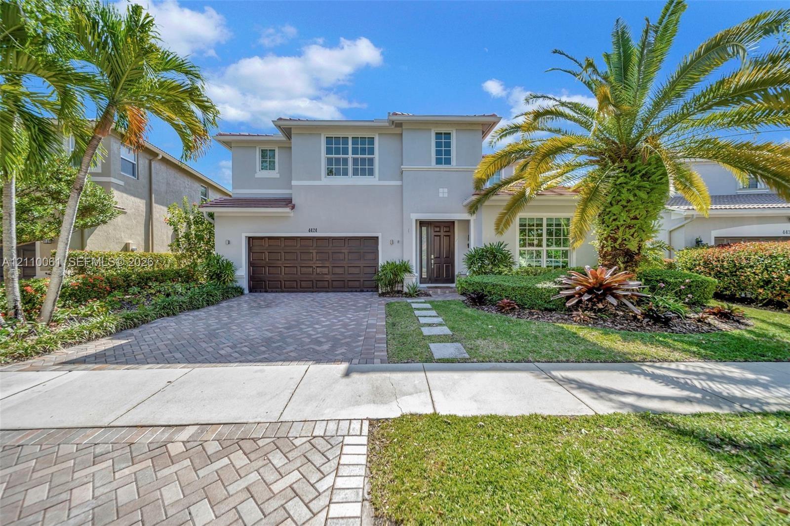 Two-story residence featuring a stucco facade, paved driveway, multi-panel garage door, and a manicured front lawn with mature palm trees