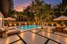 In-ground swimming pool featuring a geometric paver patio with turf inlays, mature palm landscaping, vertical wood-slat perimeter fencing, and integra