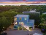 Elevated coastal residence featuring a metal roof, multi-level covered porches, and a gravel ground-level space, set against a backdrop of mature foli