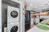 Stacked laundry unit, white cabinetry with stone countertops, stainless steel appliance suite, and open shelving