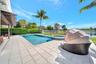Swimming pool and attached spillover spa with mosaic tile accents, extensive concrete paver pool deck, covered pergola, and perimeter metal fencing