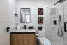 Modern vanity with a composite countertop and integrated basin, rectangular wall-mounted mirror, matte black plumbing fixtures, glass-enclosed shower,