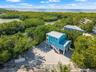 Elevated residence featuring a metal roof, exterior stairway, stone-surface driveway, and onsite storage structure, situated within proximity to coast