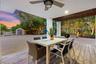 Covered patio featuring wood-finish tile flooring, ceiling fan, and exposed wood-beam detailing, opening to a gravel courtyard with a storage structur