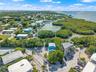 Aerial perspective featuring direct water frontage, established mangrove vegetation, and a coastal residential setting with paved road access